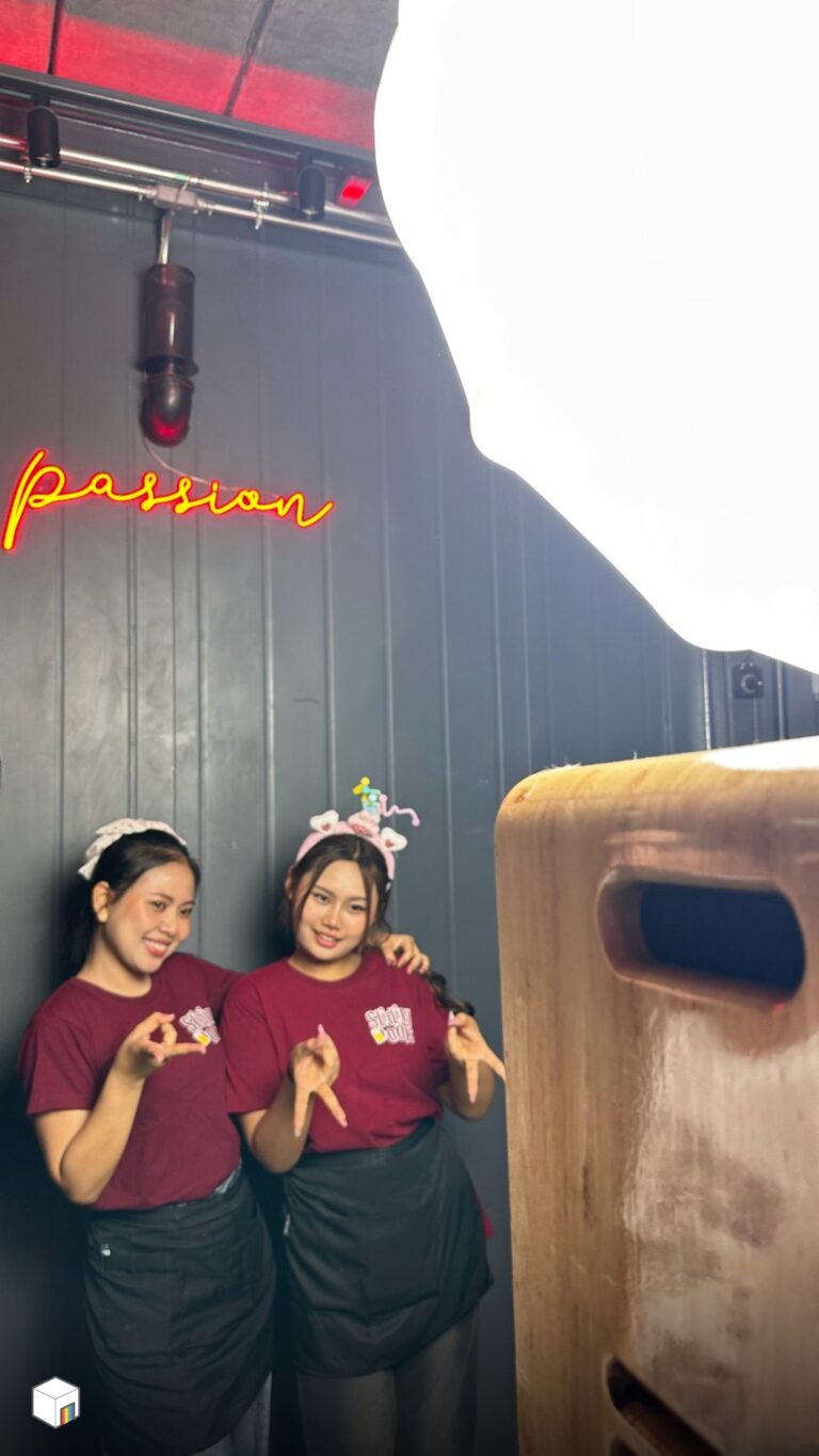 โฟโต้บูธ ผู้หญิงสองคนสวมเสื้อสีแดงโพสท่าหน้าตู้โฟโต้บูธไม้